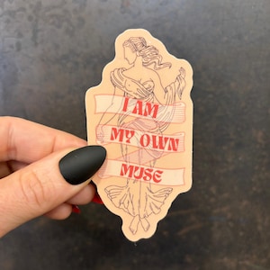 Puede incluir: Una pegatina con un dibujo lineal de una figura femenina clásica con un vestido fluido. El texto "I AM MY OWN MUSE" está impreso en rojo sobre una pancarta. La pegatina tiene un fondo melocotón claro.