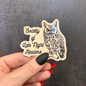 May include: A sticker featuring an owl illustration and the text "Society of Late Night Readers." The owl is perched on a branch, with detailed feather patterns. The sticker has a vintage, aged paper appearance.