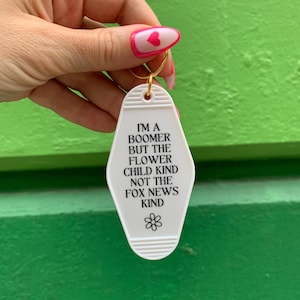 May include: White motel key chain with the text "I'm a boomer but the flower child kind not the fox news kind" and a small flower graphic.