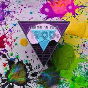 May include: A purple, pink, and blue triangle-shaped enamel pin with the text "Born in the 90s" and a retro-style grid pattern.