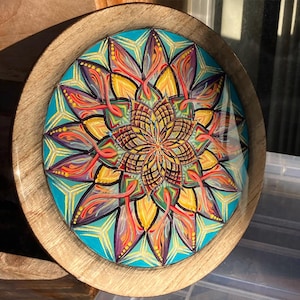 Könnte beinhalten: Ein rundes Holztablett mit einem farbenfrohen Mandala-Design, das auf die Oberfläche gemalt ist. Das Mandala zeigt komplizierte Muster in Rot-, Orange-, Gelb-, Grün-, Blau- und Violetttönen.