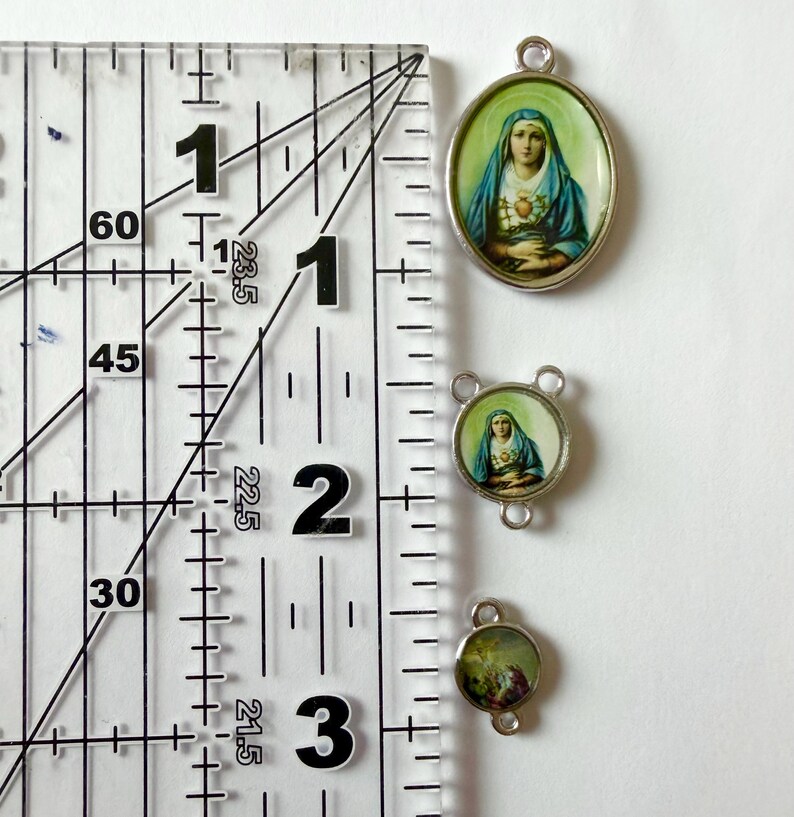 Pu&ograve; includere: Tre ciondoli religiosi con montatura color argento. Il pi&ugrave; grande &egrave; ovale, quello centrale &egrave; rotondo con tre anelli e il pi&ugrave; piccolo &egrave; rotondo. Ogni ciondolo presenta un'immagine religiosa. Il righello mostra che i ciondoli misurano circa 2,5 cm, 1,9 cm e 1,3 cm.