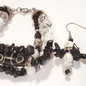May include: A black and white beaded bracelet and matching earrings set. The bracelet features black and white beads, a large black and white stone, and silver accents. The earrings are made with the same black and white beads and silver accents.