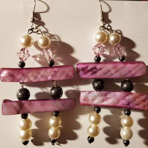 May include: A pair of dangle earrings with pink and white shell beads, clear crystal beads, and silver hooks.