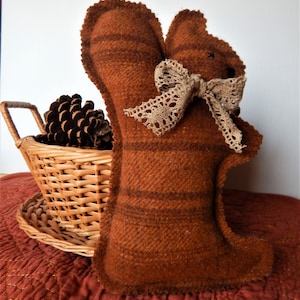 May include: A brown and orange striped fabric squirrel with a brown lace bow. The squirrel is sitting on a red and gold fabric surface.