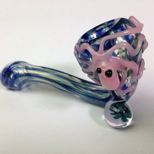 May include: A glass pipe with a blue and white swirl design. The bowl of the pipe is shaped like an octopus with pink tentacles and black eyes.