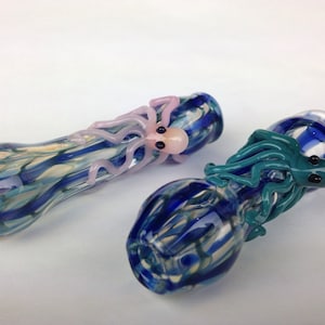 May include: Two glass pipes with blue and white swirl designs. One pipe has a pink octopus attached to it, and the other has a blue octopus attached to it.