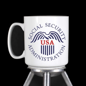 May include: White ceramic mug with a blue and red Social Security Administration logo featuring an eagle and the words "Social Security Administration USA".