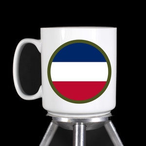 May include: White ceramic mug with a blue, white, and red circle design on the front. The circle is outlined in green and has a white background.