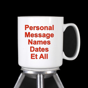 Puede incluir: Taza de cer&aacute;mica blanca con una inscripci&oacute;n roja que dice "Personal Message Names Dates Et All". La taza est&aacute; sobre un soporte plateado con tres patas.