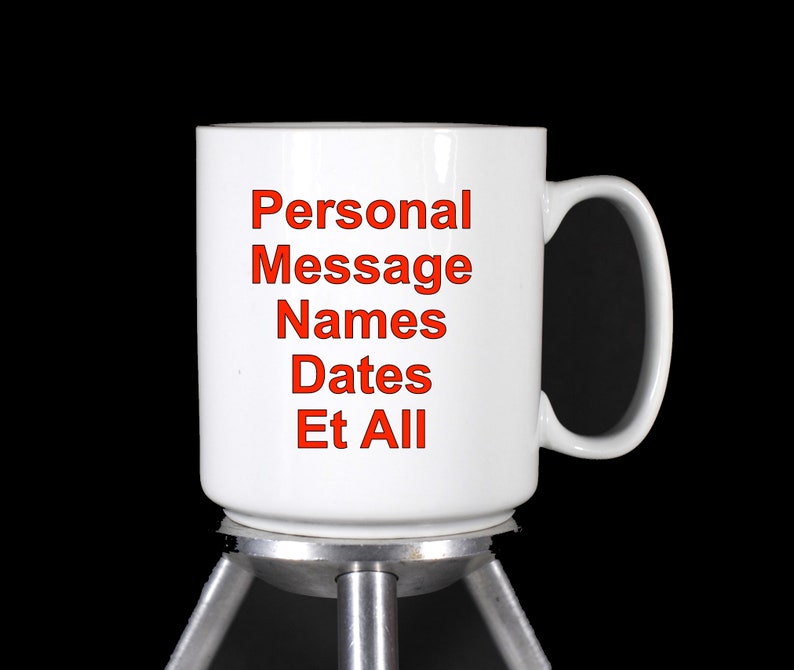 Puede incluir: Taza de cer&aacute;mica blanca con una inscripci&oacute;n roja que dice "Personal Message Names Dates Et All". La taza est&aacute; sobre un soporte plateado con tres patas.