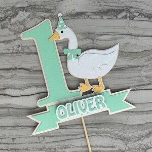 First birthday cake topper with a goose and personalized with the name Oliver.  Shown in the mint green accent color.
