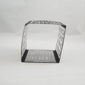 May include: A black and white paper box with the word "CONGRATULATIONS" printed on the inside and outside. The box is rectangular with a clear, transparent base. The box is angled slightly.
