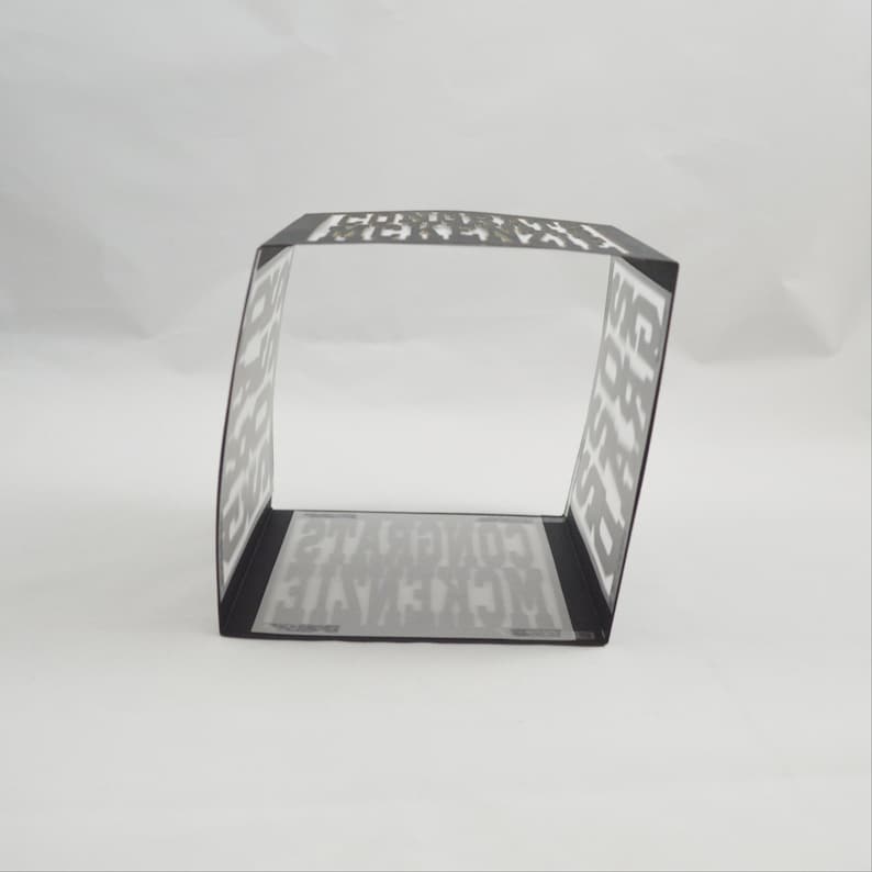 May include: A black and white paper box with the word "CONGRATULATIONS" printed on the inside and outside. The box is rectangular with a clear, transparent base. The box is angled slightly.