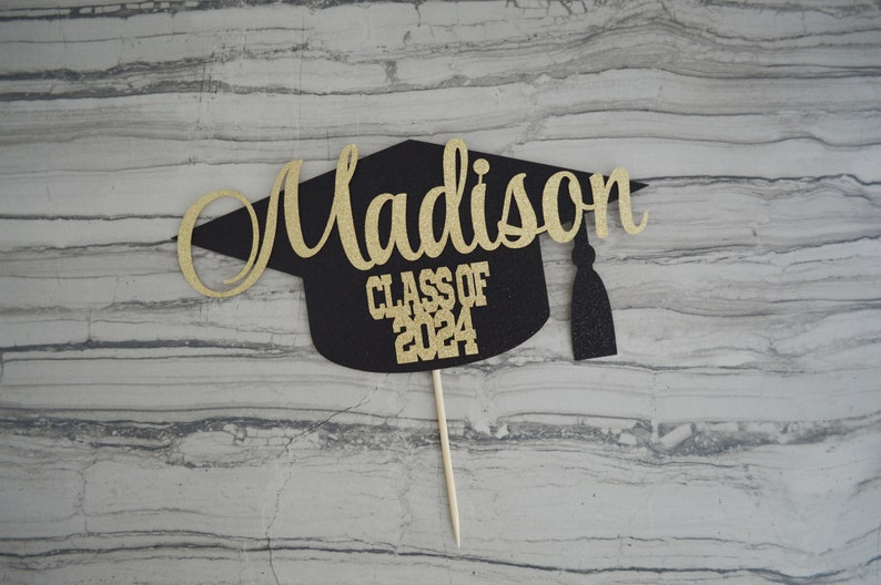 Graduation cap shape glitter cake topper personalized with name across the top and Class of 2024 along the bottom.