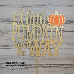 Puede incluir: Adorno para tarta con purpurina dorada con la frase "A little PUMPKIN is on the WAY" y una calabaza naranja. El adorno est&aacute; sujeto a un palito de madera para insertarlo f&aacute;cilmente en una tarta.