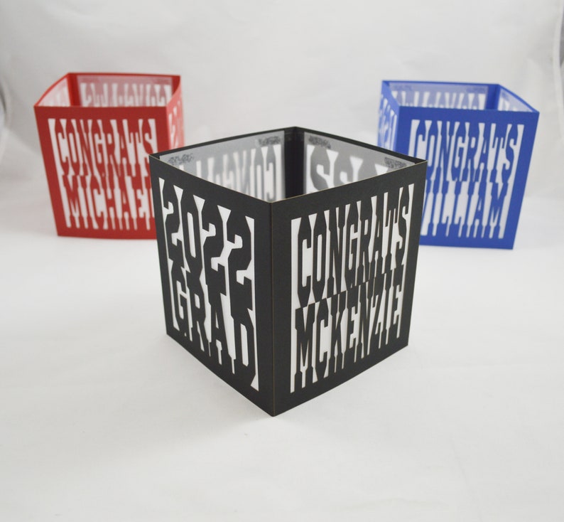 May include: A set of three ceramic mugs with a speckled, cream-coloured glaze. Each mug features a different hand-painted floral design in shades of blue, green, and yellow. The mugs have a simple, modern shape.