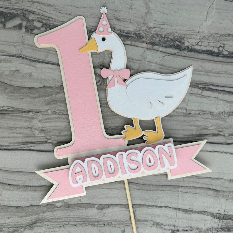 First birthday cake topper with a goose and personalized with the name Addison.  Shown in the light pink accent color.