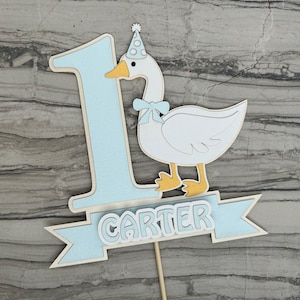 First birthday cake topper with a goose and personalized with the name Carter.  Shown in the light blue accent color.