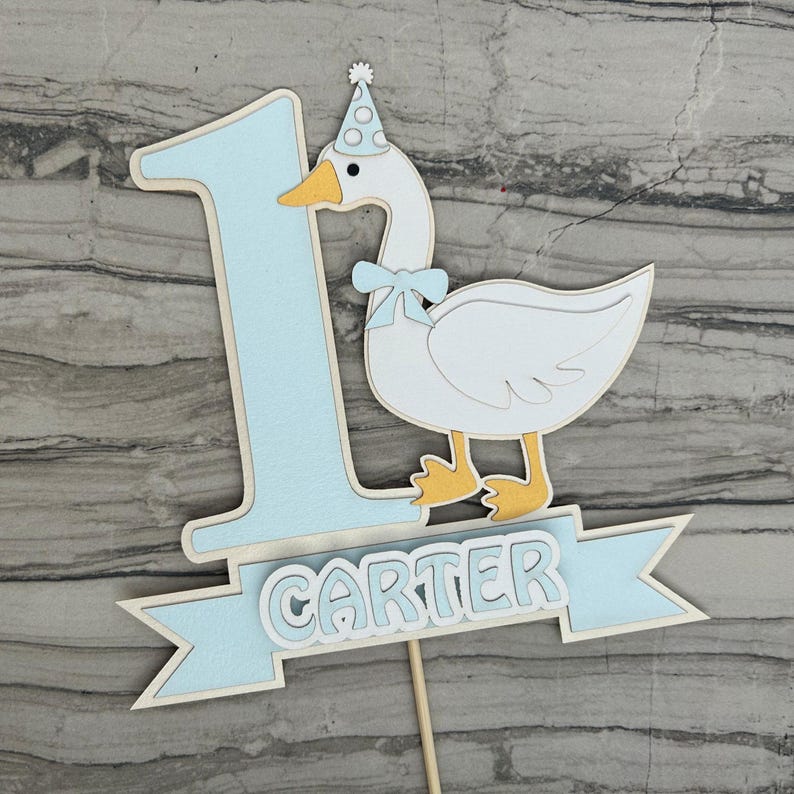 First birthday cake topper with a goose and personalized with the name Carter.  Shown in the light blue accent color.