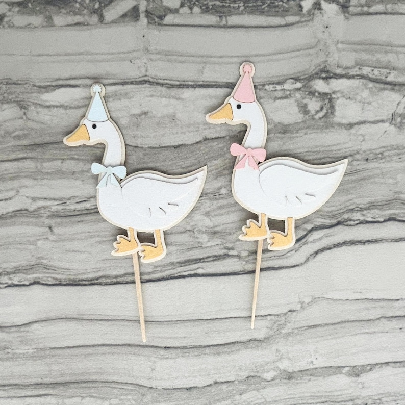 Two goose cupcake toppers shown in light pink and light blue accent color options.