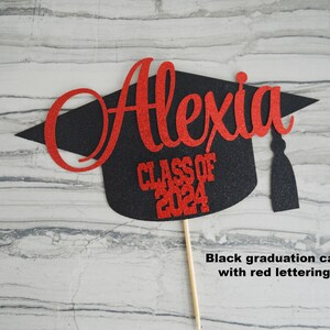 Graduation cap shape glitter cake topper personalized with name across the top and Class of 2024 along the bottom. Shown here with the name Alexia in red glitter on a black graduation cap.