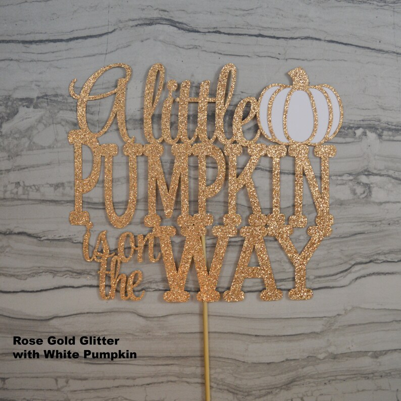 Puede incluir: Adorno para tarta de purpurina oro rosa con la frase "A little PUMPKIN is on the WAY" y un dise&ntilde;o de calabaza blanca. El adorno est&aacute; sujeto a un palito de madera.