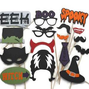 May include: A collection of Halloween-themed photo booth props on wooden sticks. Includes speech bubbles with "EEK" and "BOO", glasses, mustaches, a witch hat, and a "WITCH" sign. The props are in black, orange, green, and purple.