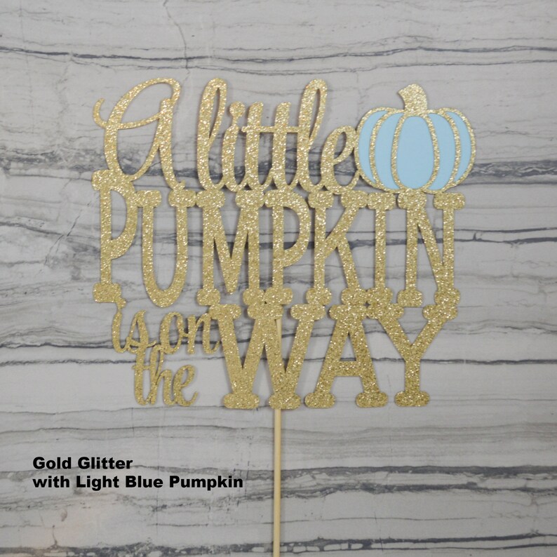 Puede incluir: Adorno dorado con purpurina para tarta con la frase "A little PUMPKIN is on the WAY" y una calabaza azul claro. El adorno est&aacute; sujeto a un palito de madera. Perfecto para un baby shower.