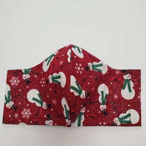 May include: Red fabric face mask with a repeating pattern of white snowmen with green scarves and black hats on a red background with white snowflakes.
