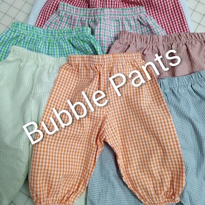 May include: A collection of bubble pants in various colors and gingham patterns. The pants are in shades of red, green, orange, and blue. The text "Bubble Pants" is overlaid on the image.