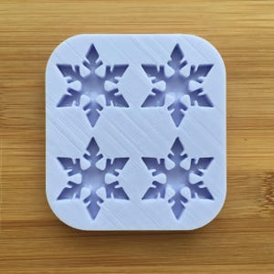 Op de afbeelding: Een lichtblauwe siliconen mal met vier sneeuwvlokvormen. De mal is ontworpen om kleine, decoratieve sneeuwvlokken te maken.