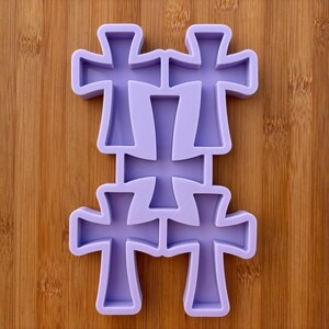 Può includere: Uno stampo in silicone viola chiaro con sei forme a croce. Lo stampo è progettato per creare più croci contemporaneamente. Le croci sono disposte in un motivo impilato, con due croci nelle file superiori e inferiori e due croci nella fila centrale.
