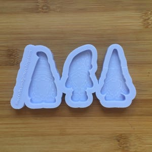 Puede incluir: Un molde de silicona con tres formas de gnomos. El molde es de color morado claro y tiene una superficie lisa. Los gnomos llevan sombreros y tienen barbas.