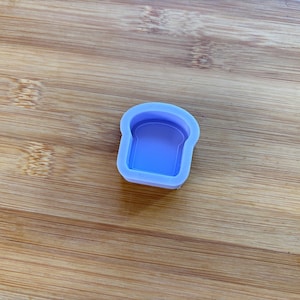 Può includere: Uno stampo in silicone azzurro a forma di fetta di pane, con un interno dettagliato. Lo stampo è posto su uno sfondo di legno, che ne evidenzia la forma e il design. Questo articolo è probabilmente per l'artigianato o la cottura.