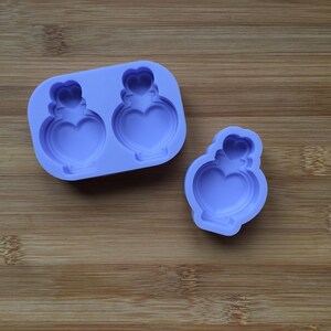 May include: A purple silicone mould with two heart-shaped bottle designs. The mould is on a wooden surface.