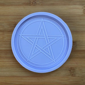 Pode incluir: Uma base para copos circular lilás claro com um design de pentagrama em relevo no centro. A base para copos tem uma borda elevada e o texto "thecraftsandglittershop.com" é impresso na borda.