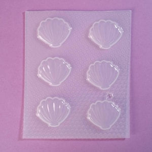 Op de afbeelding: Een transparante plastic mal met zes afzonderlijke holtes in de vorm van schelpen. De mal is ontworpen voor het maken van kleine, decoratieve items zoals zeep, hars of snoep.