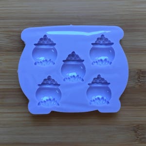 May include: Purple silicone mould with five cauldron shapes. Each cauldron has a raised design of gold coins.