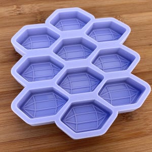 Pode incluir: Uma forma de silicone roxo com 10 cavidades hexagonais, cada uma com um design geométrico em relevo. A forma é projetada para fazer artesanato de resina.