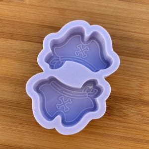 Puede incluir: Molde de silicona morado con dos formas de campana. Cada campana tiene un diseño de cruz.