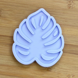 Può includere: Uno stampo in silicone color lavanda chiaro a forma di foglia di monstera. Lo stampo presenta un bordo esterno rialzato e ritagli interni che definiscono il caratteristico motivo a foglia divisa della pianta, creando un design incavato per progetti di colata.