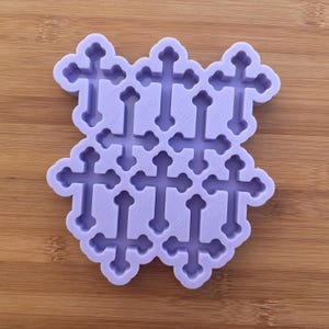 Può includere: Uno stampo in silicone lilla chiaro con una griglia di undici croci. Le croci hanno un design tradizionale con estremità svasate. Lo stampo è posto su uno sfondo di legno.