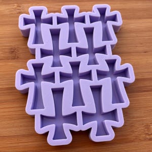 Può includere: Un gruppo di stampi a forma di croce di colore viola chiaro. Gli stampi sono realizzati in un materiale flessibile e sono disposti in un motivo a strati. Le croci hanno un design semplice e simmetrico, con bordi arrotondati. Lo sfondo è una superficie di legno.
