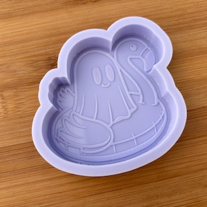 May include: A light purple silicone mold featuring a cartoon ghost floating on a flamingo pool float. The ghost has a friendly expression with two oval eyes and a smiling mouth. The mold is designed for crafting.