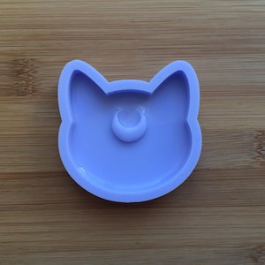 May include: A light purple silicone mould shaped like a cat's face with a crescent moon in the centre.