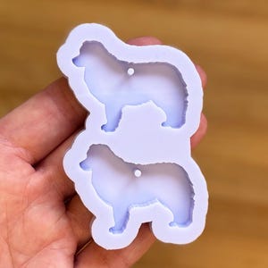 Op de afbeelding: Een lichtpaarse siliconen mal met twee honden silhouetten. Elke hond heeft een pluizige staart en een klein gaatje om op te hangen. De mal is ontworpen voor het knutselen en creëren van honden-vormige items.