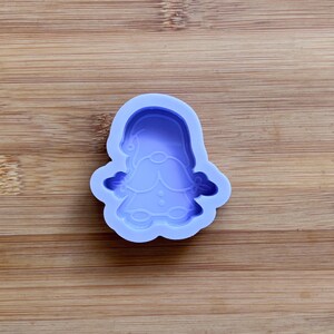 Puede incluir: Un molde de silicona lavanda con forma de gnomo. El molde presenta un diseño detallado del sombrero, la barba y la ropa del gnomo. El molde está diseñado para la elaboración y creación de artículos decorativos.