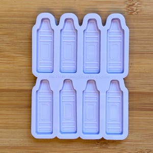 Peut inclure: Un moule en silicone violet clair comportant huit cavités en creux en forme de crayons, disposées en deux rangées de quatre. Le texte thecraftandglittershop.com est gravé au centre du moule entre les deux rangées d'empreintes en forme de crayon.