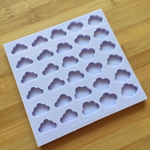 May include: A purple silicone mould with 30 cloud-shaped cavities. The mould is on a wooden surface. The text "thecraftsandglittershop.com" is printed on the bottom right corner of the mould.